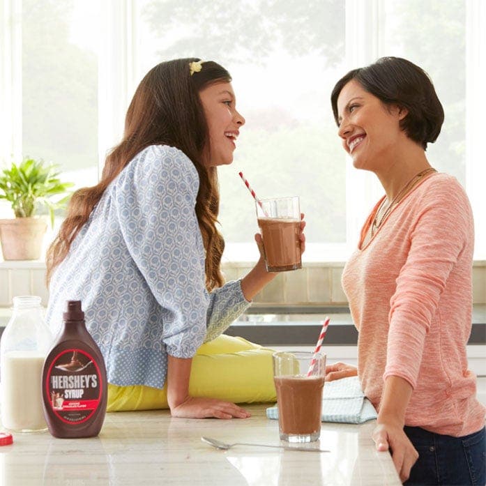 mother and daughter standing near the table and enjoying hersheys syrup shake